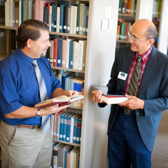 Two male professor in the library taking with books in their hands.
